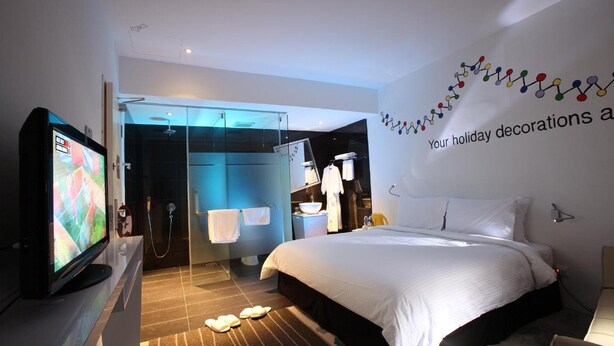 A modern hotel room with a large bed, a TV, a shower area, and holiday decorations on the wall.