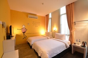 Quarto de hotel com duas camas, uma mesa com telefone e chaleira, e uma parede com uma frase motivacional.