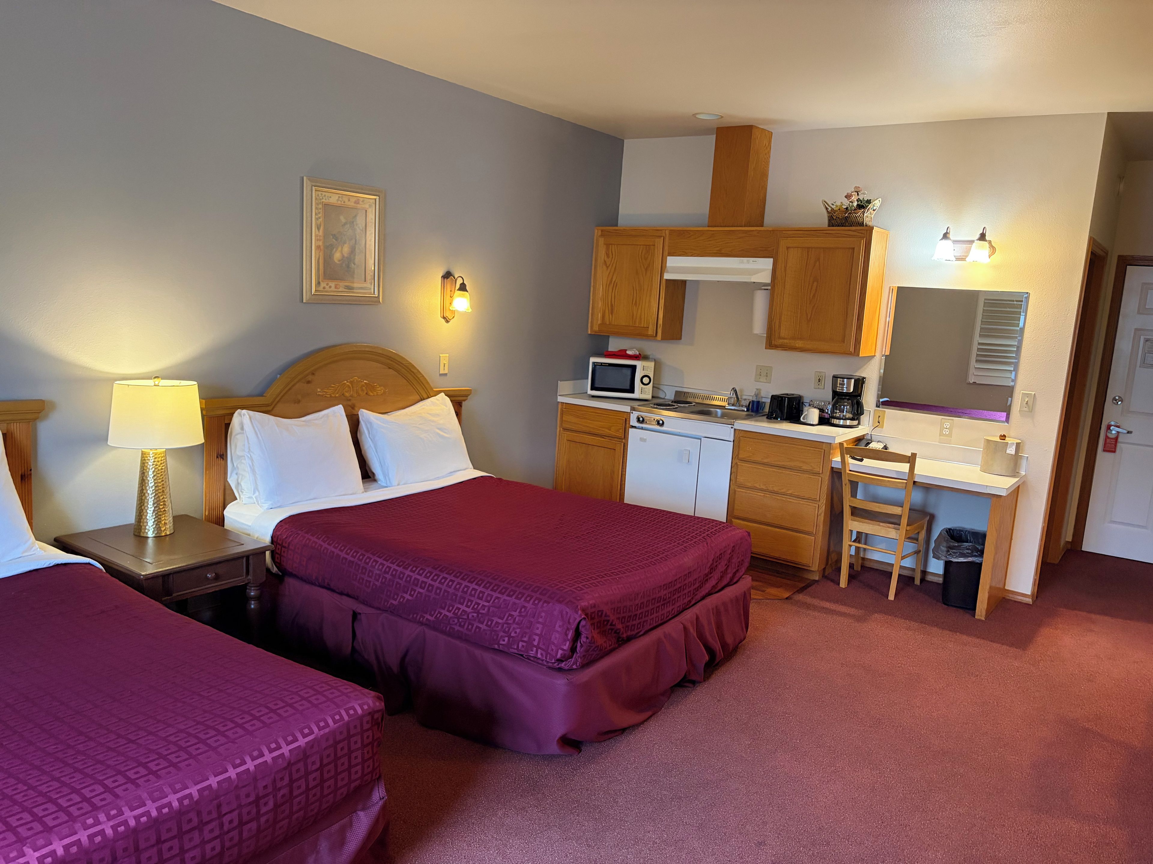Ett hotellrum med två sängar, ett litet pentry, en mikrovågsugn, en kaffebryggare och ett litet skrivbord med en stol.