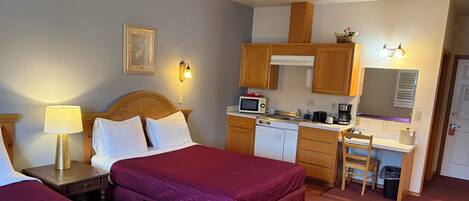 Habitación de hotel con dos camas, kitchenette, microondas, cafetera y escritorio pequeño con silla.