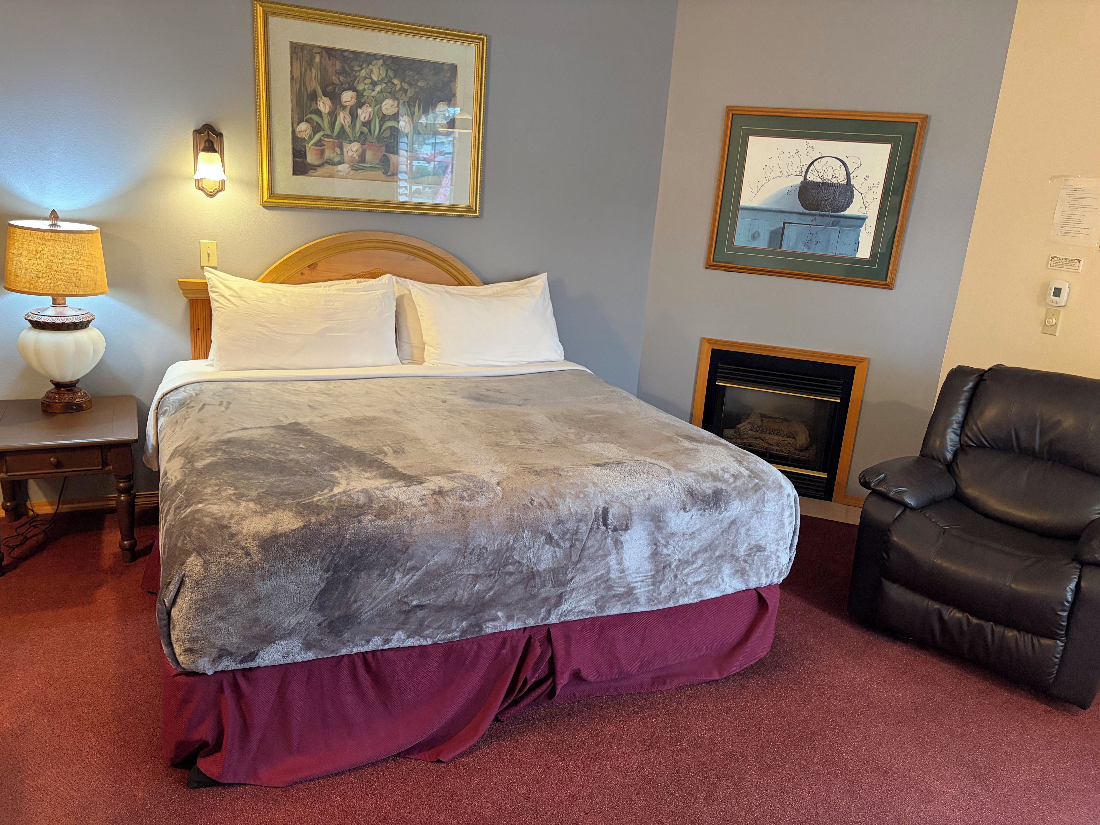 A hotel room with a large bed, a chair, a lamp, and two framed pictures on the wall.