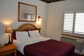 A neatly made bed with a wooden headboard, a bedside lamp, and a framed artwork on the wall.
