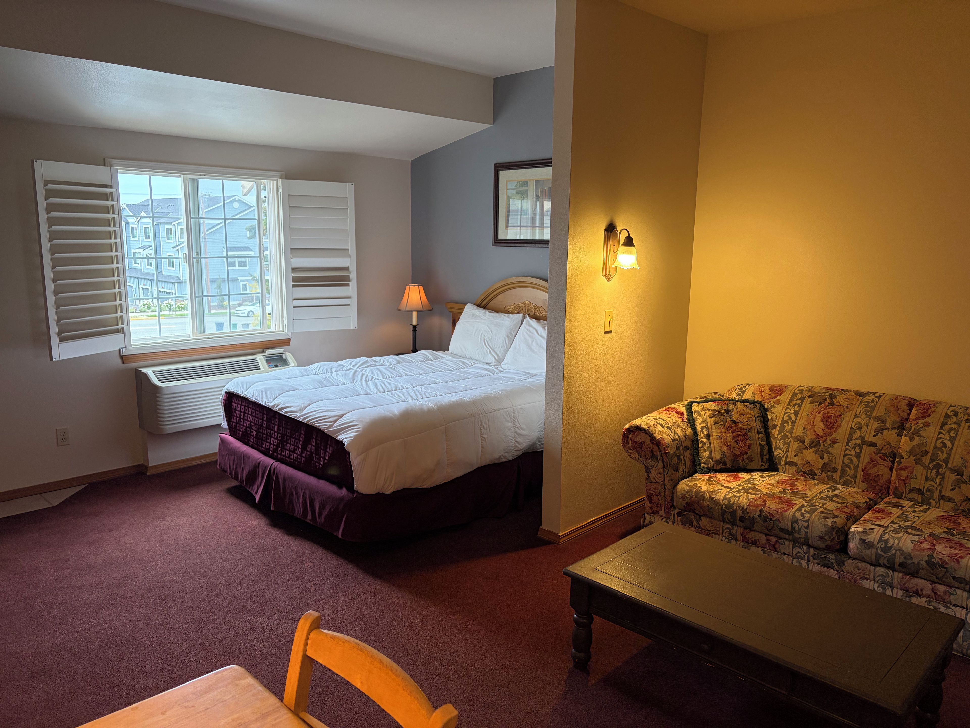 Habitación de hotel con cama, sofá, mesa y ventana con persianas.