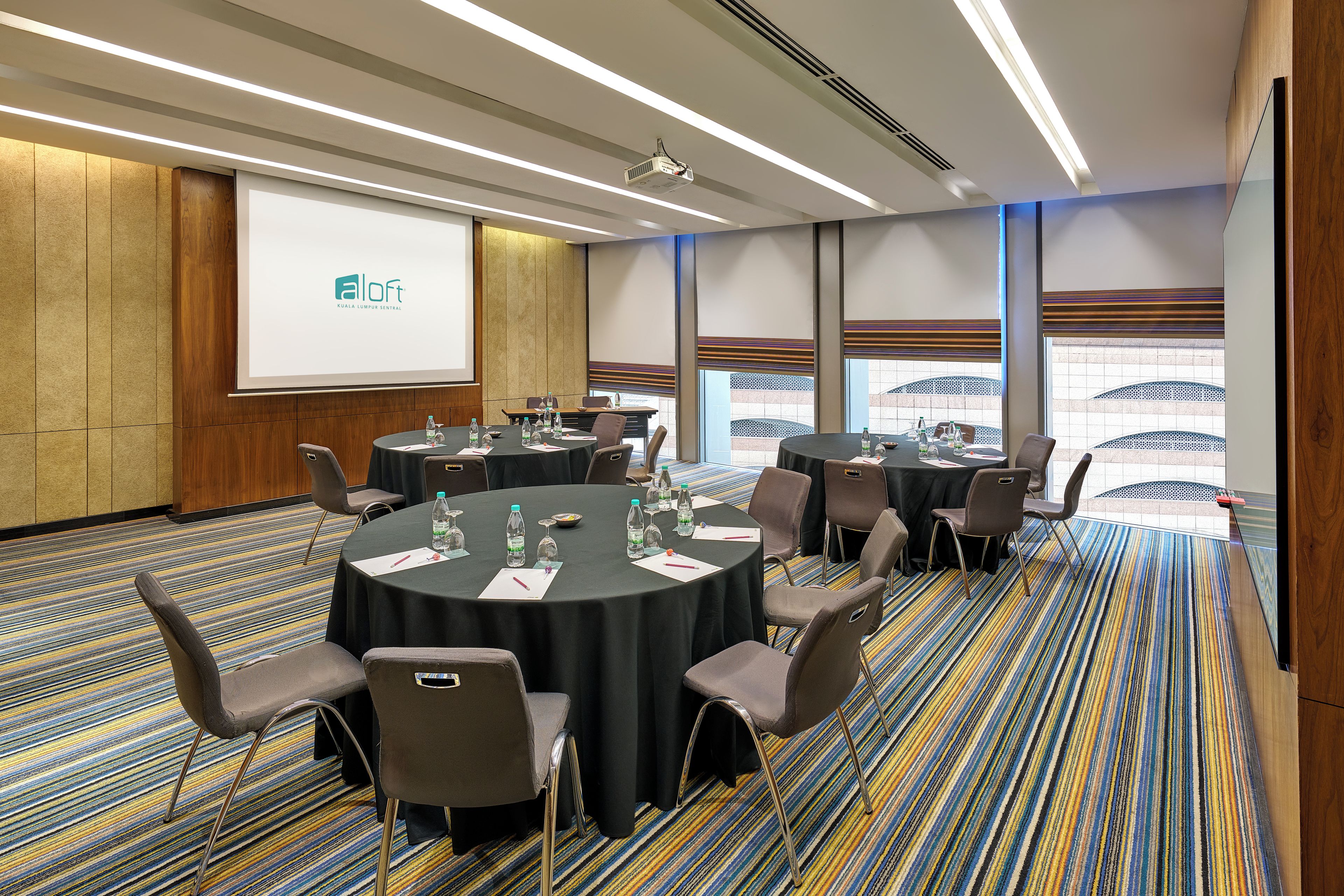 A conference room with round tables, chairs, and a projector screen.