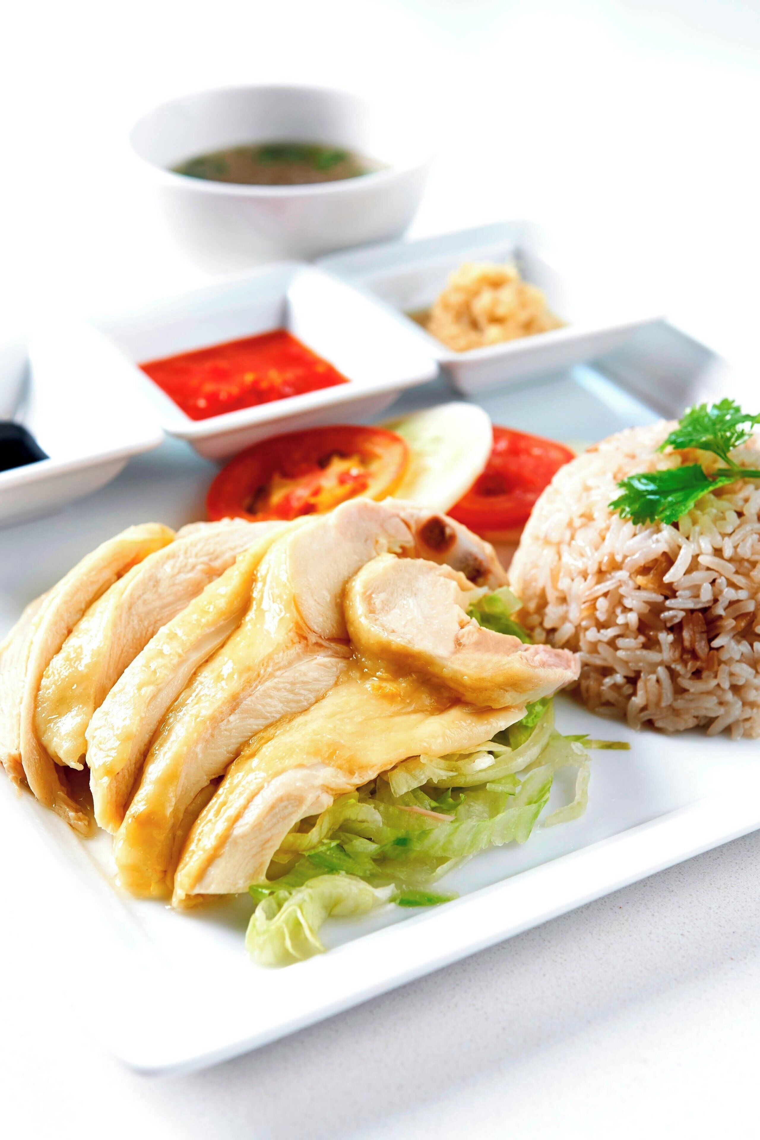 A plate of sliced chicken, rice, and vegetables with condiments.