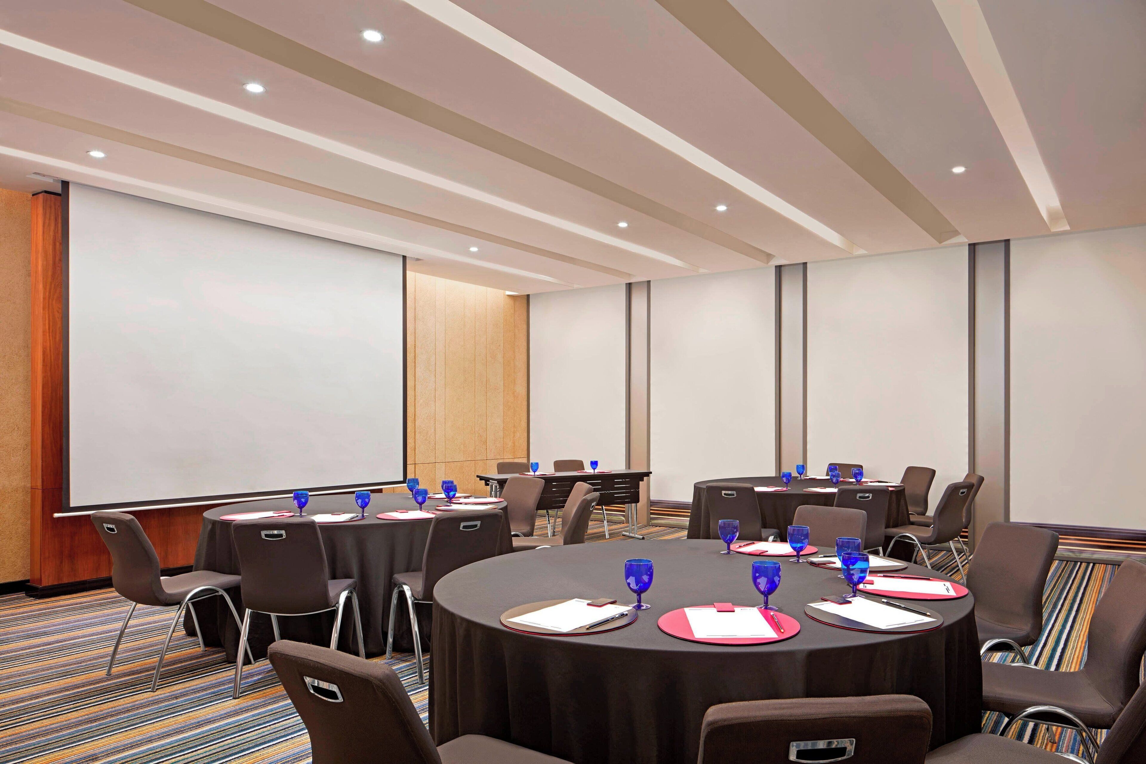 A conference room with round tables, chairs, and a projection screen.