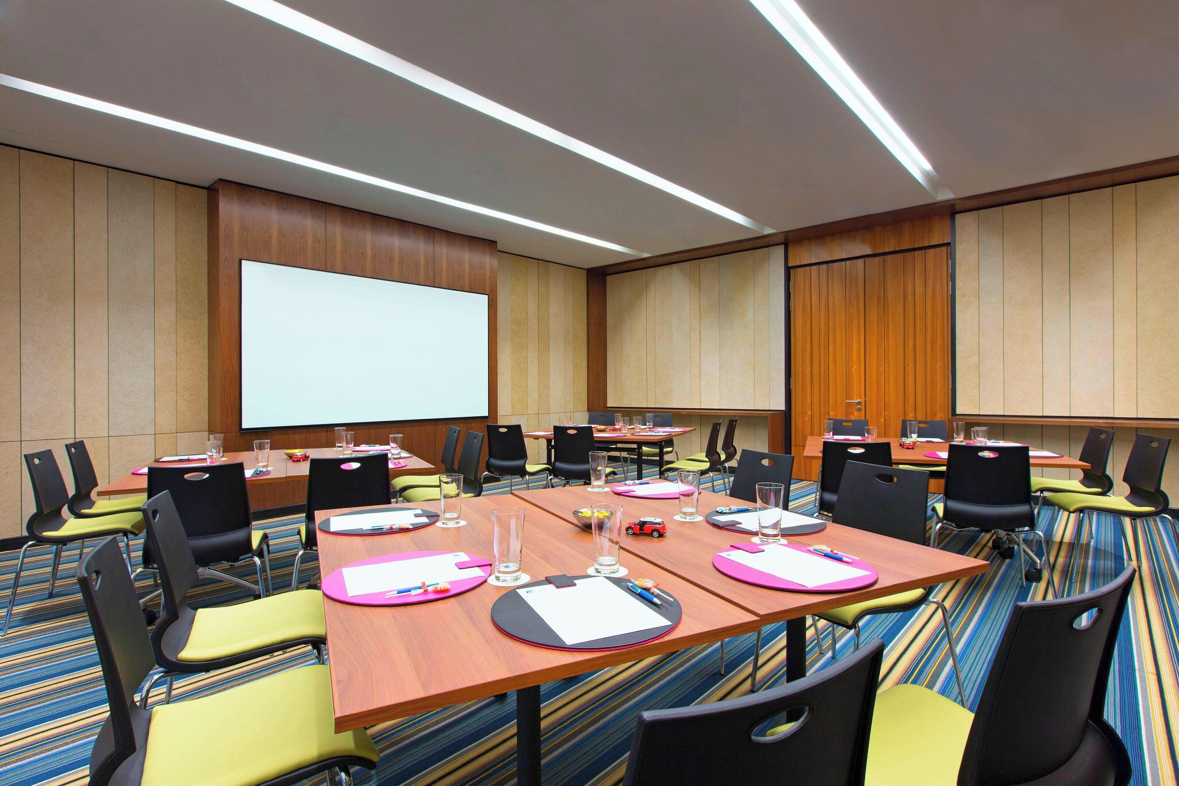 A conference room with multiple tables, chairs, and a large screen.
