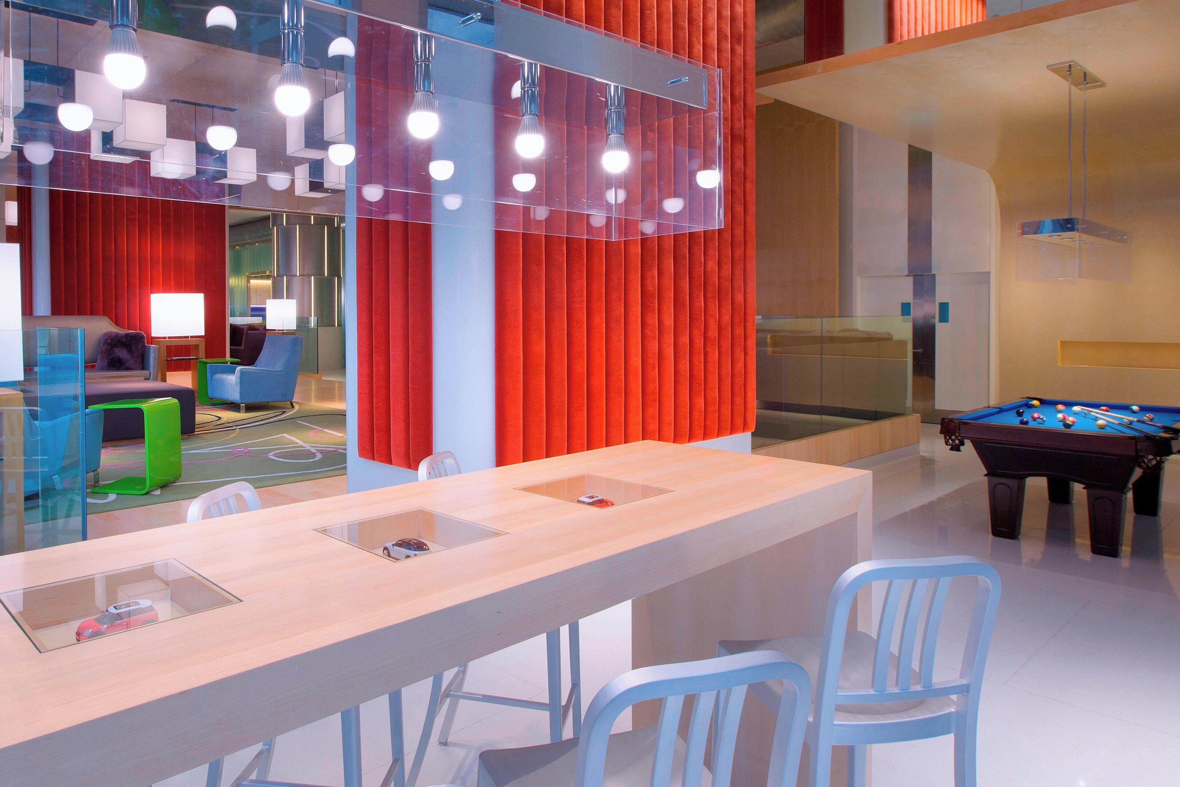 A modern indoor space with a pool table, seating area, and a bar with a glass-top counter.