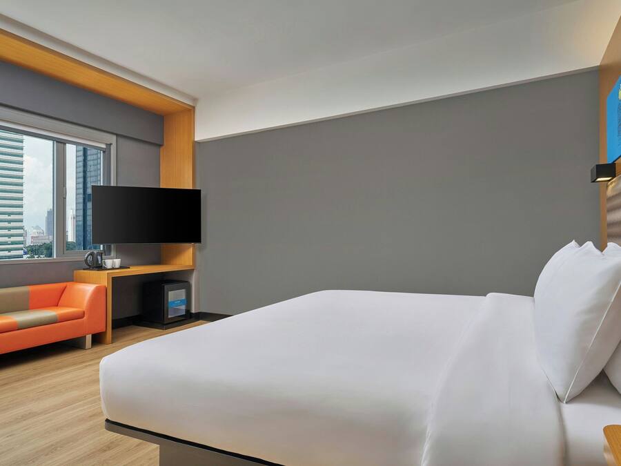 Ein modernes Hotelzimmer mit einem großen Bett, einer Sitzecke, einem Flachbildfernseher und Blick auf die Stadt.