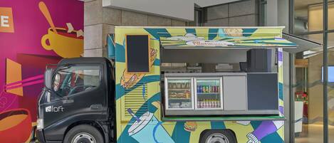 Un colorato furgone cibo con un taxi nero parcheggiato di fronte a un edificio con un vivace murale.