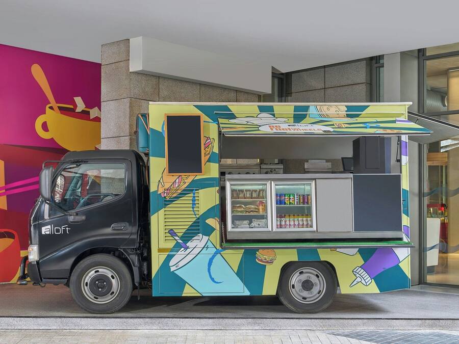 Un camión de comida colorido con un taxi negro estacionado frente a un edificio con un mural vibrante.