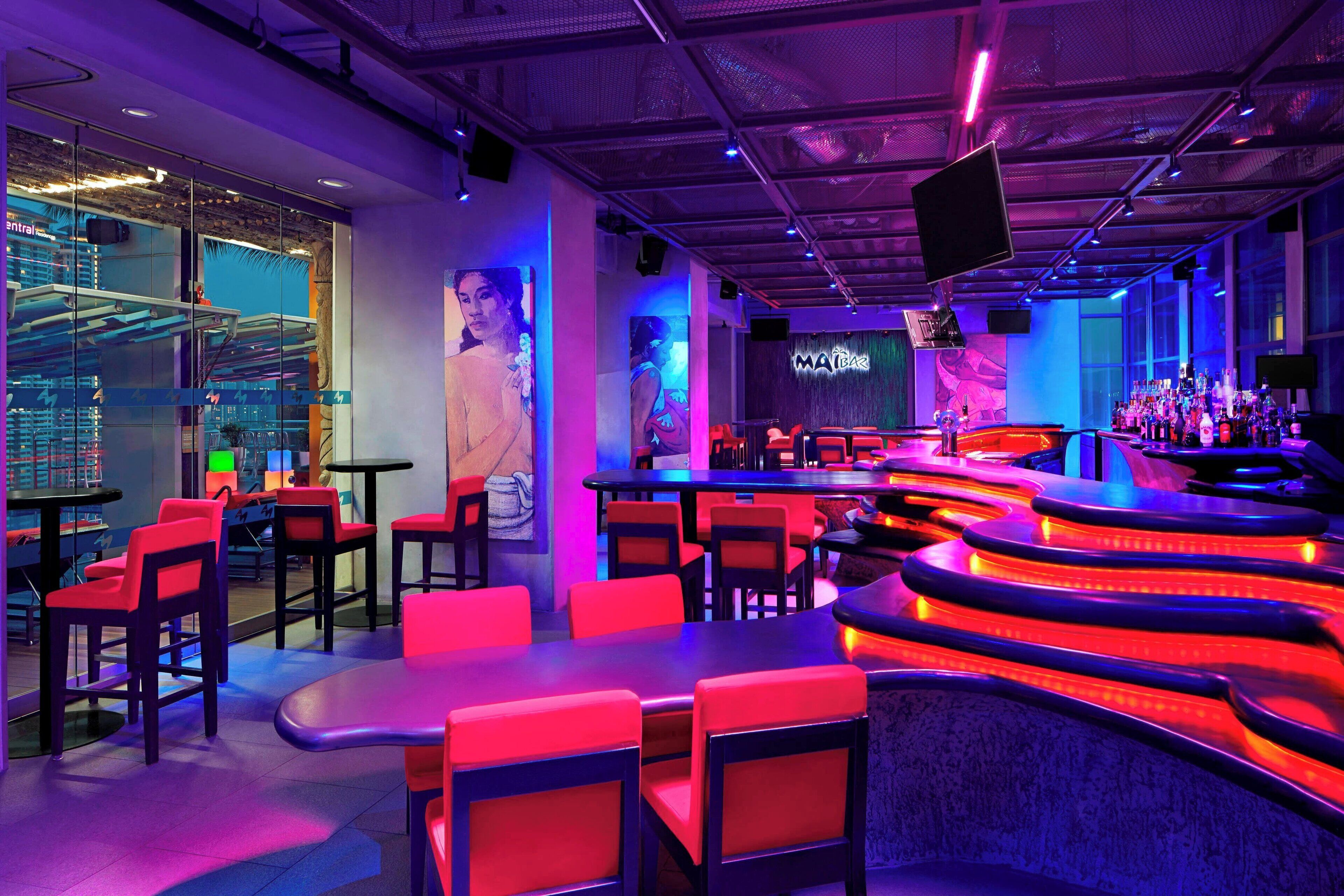 A bar area with red and black seating, a counter with a neon sign, and a mural on the wall.