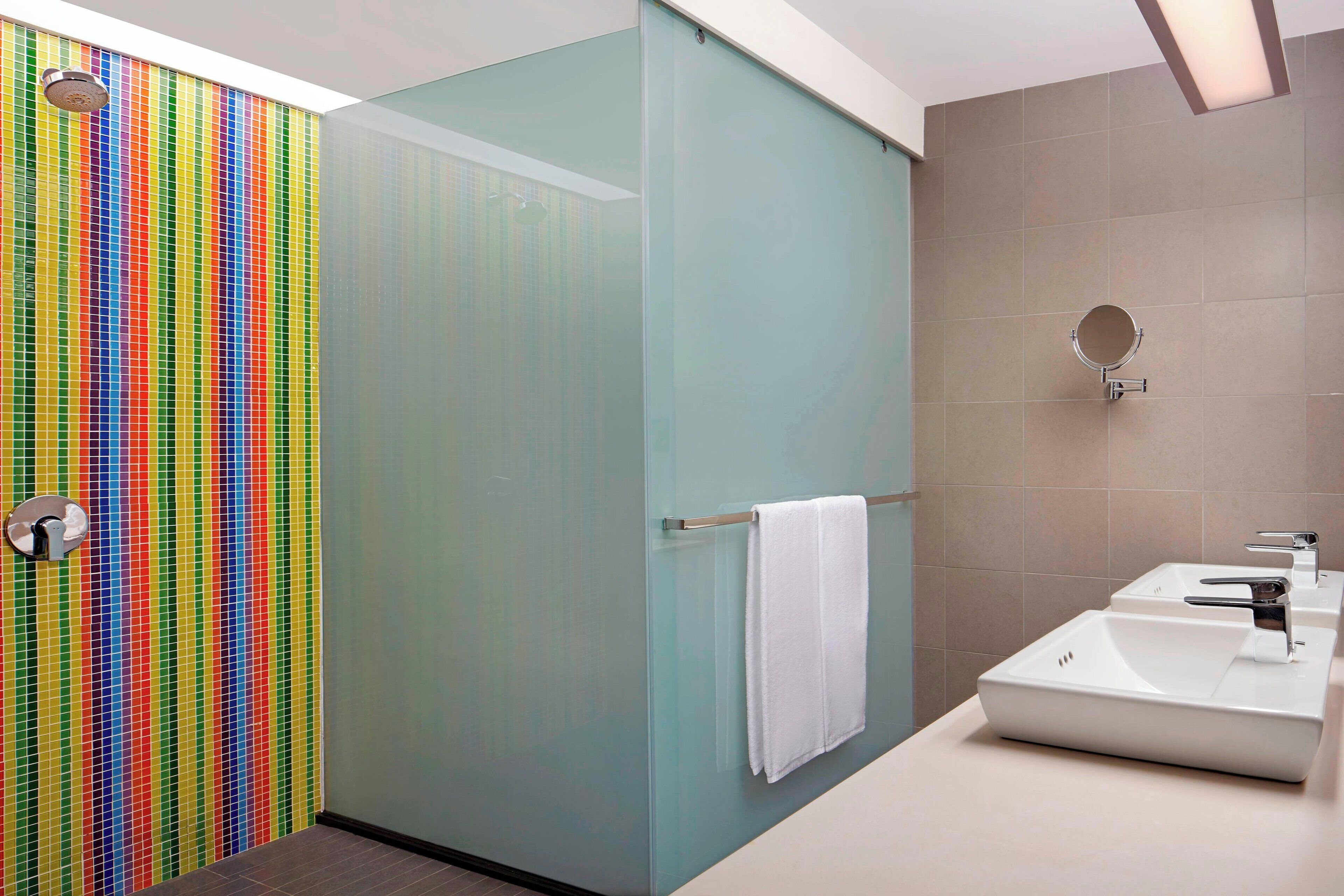A modern bathroom with a glass shower enclosure, a white towel hanging on the door, and a sink with a mirror.
