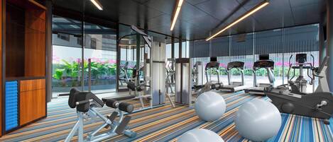 Une salle de sport moderne, équipée de matériel d’exercice, dotée d’un tapis à motifs et de grandes fenêtres donnant sur un paysage verdoyant.