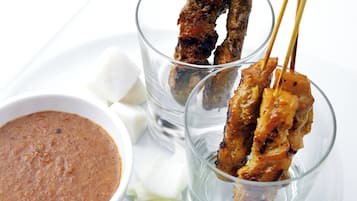 Brochetas de carne a la parrilla con salsa para mojar y rodajas de pepino sobre un plato blanco.