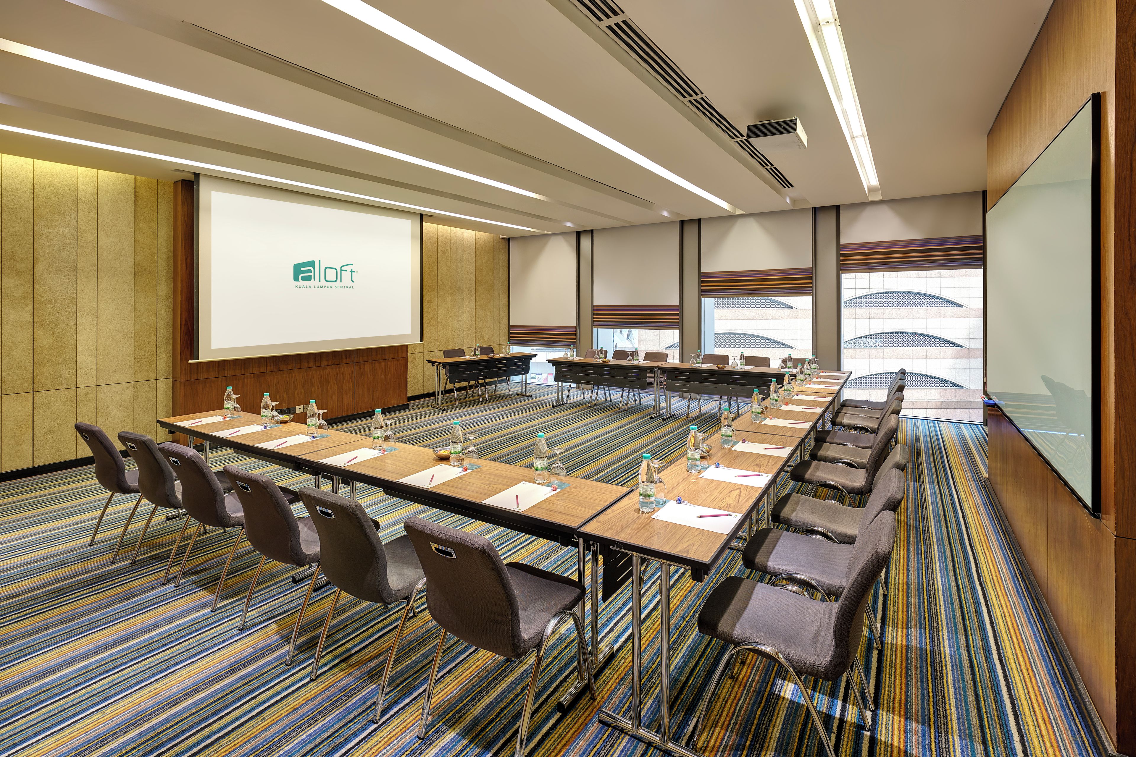 A conference room with a long table, chairs, a projector screen, and a carpeted floor.