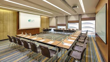 A conference room with a long table, chairs, a projector screen, and a carpeted floor.