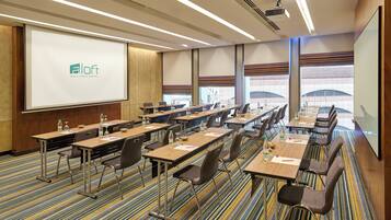 A conference room with a presentation screen, multiple tables with chairs, and a carpeted floor.