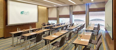A conference room with a presentation screen, multiple tables with chairs, and a carpeted floor.