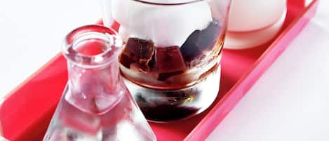 Un vaso de café helado con pajita rosa, una botella de leche y una jarra pequeña sobre una bandeja roja.