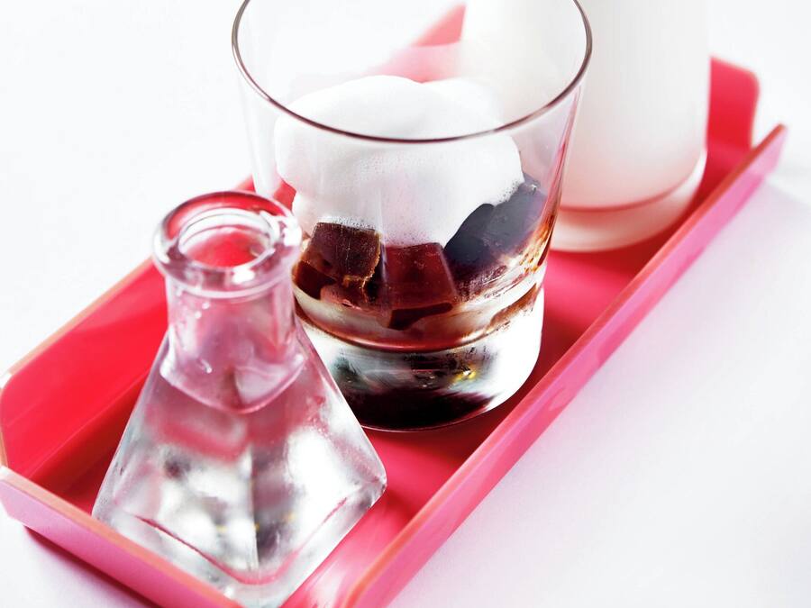 Un vaso de café helado con pajita rosa, una botella de leche y una jarra pequeña sobre una bandeja roja.