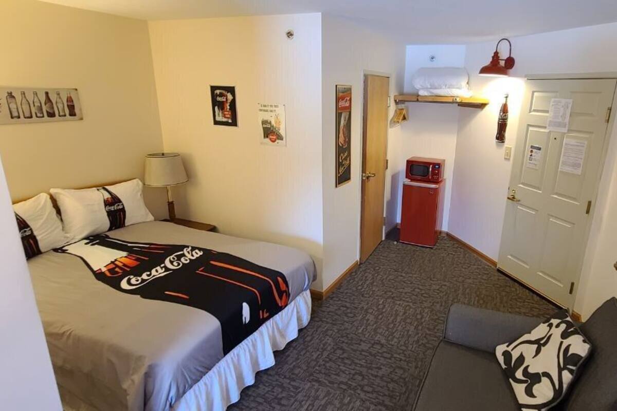 A compact hotel room with a bed, a sofa, a microwave, and a television.