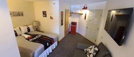 A compact hotel room with a bed, a sofa, a microwave, and a television.