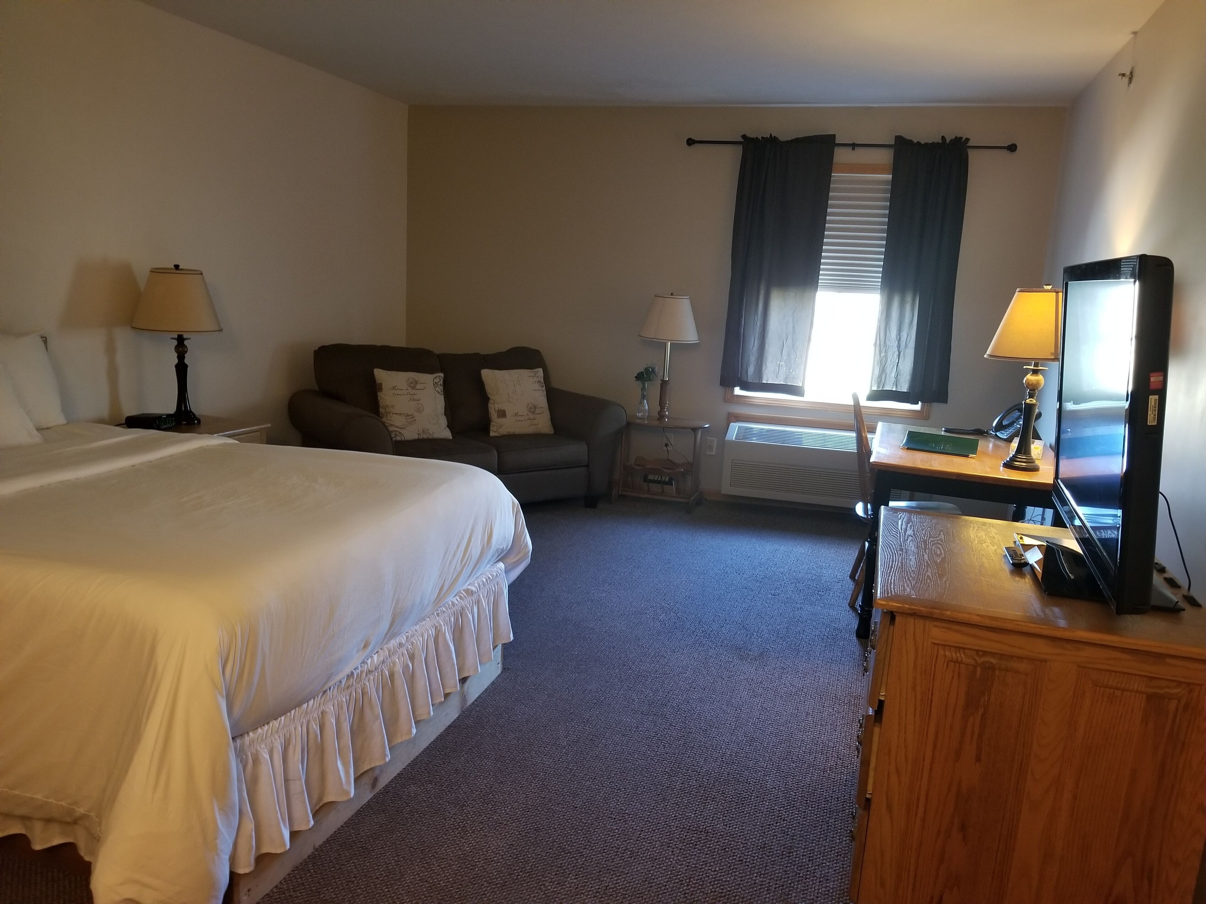 A hotel room with a large bed, a desk with a computer, a television, and a sofa with decorative pillows.