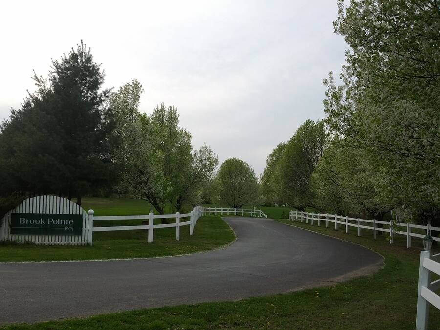 Une route menant à l’auberge Brook Pointe, bordée d’une clôture blanche et d’arbres des deux côtés.