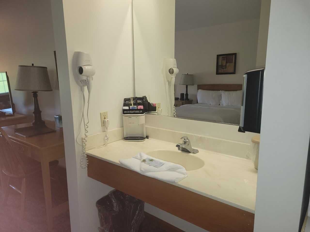 Un baño de hotel con lavamanos, espejo, secador de pelo y toalla.