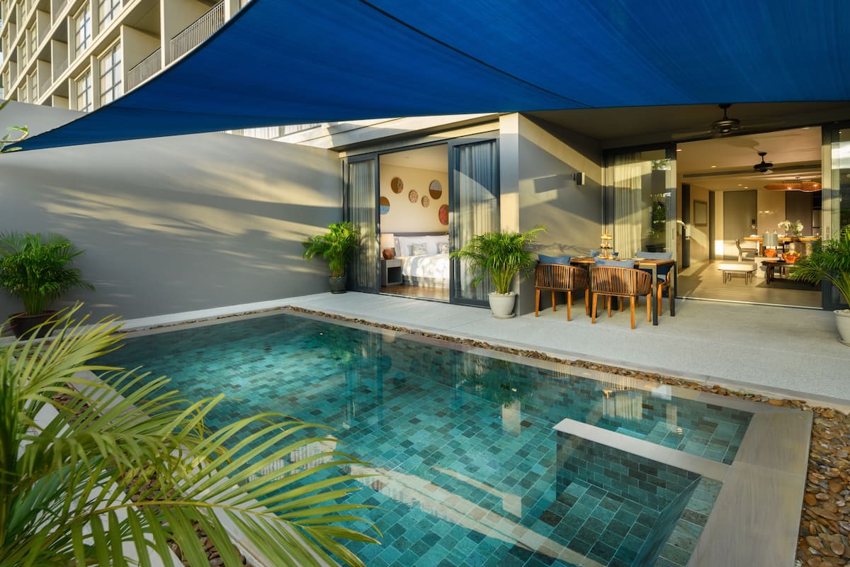Un espace piscine moderne doté d’un patio fermé par des baies vitrées, d’un coin repas avec mobilier d’extérieur et d’une vue sur l’immeuble voisin.