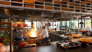 Un chef cocina sobre fuego en una cocina moderna con estantes de madera y ventanas amplias.