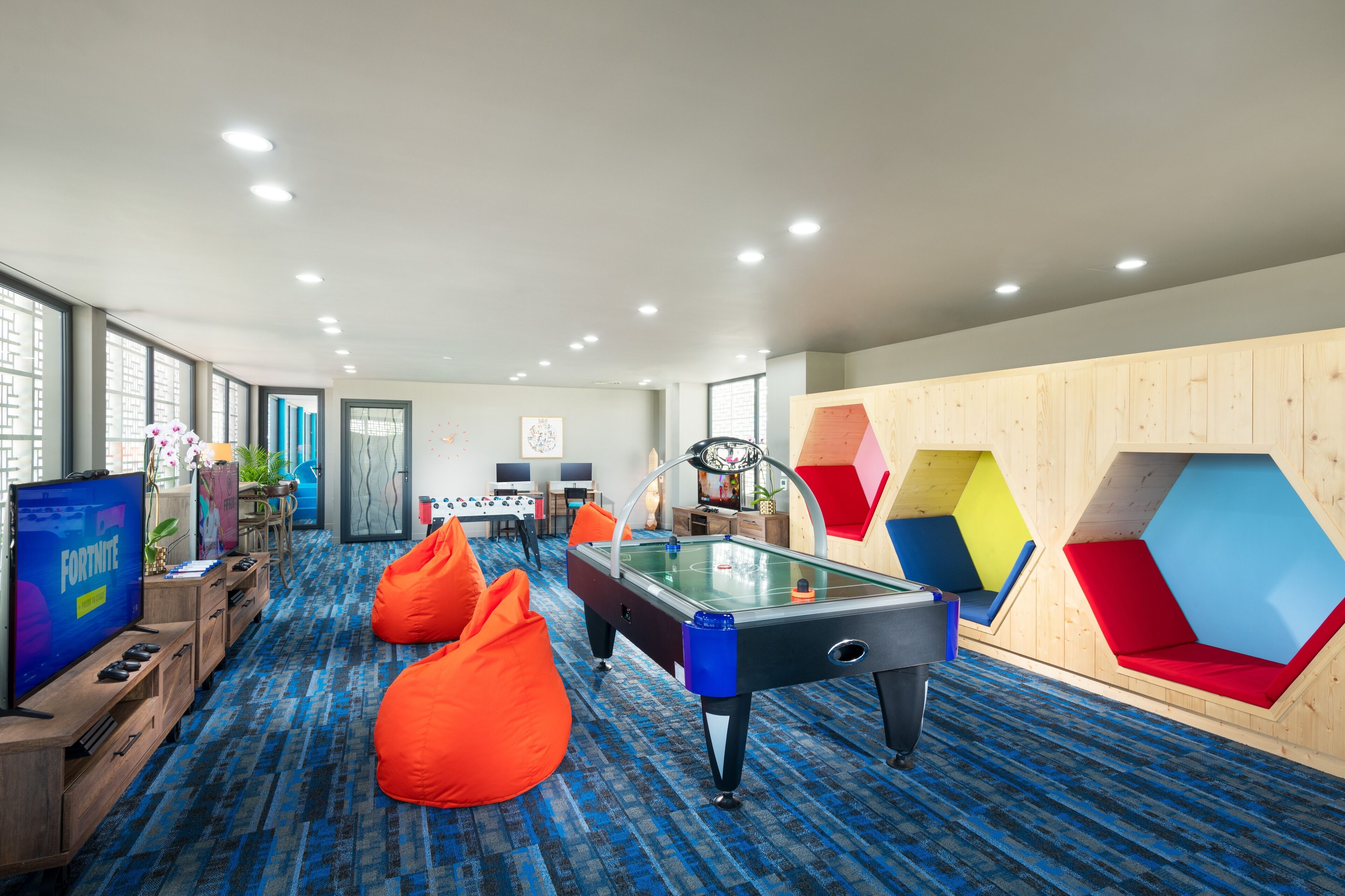 A modern indoor recreational area with a foosball table, bean bags, and a large screen displaying a video game.