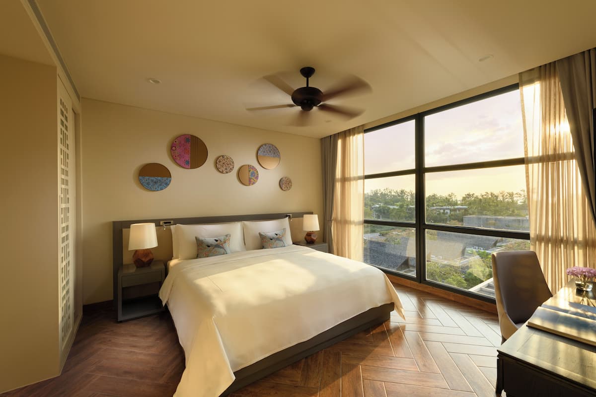 Une chambre d’hôtel dotée d’un grand lit, d’un ventilateur de plafond, d’une vue sur la ville et d’un coin repas avec une table et des chaises.