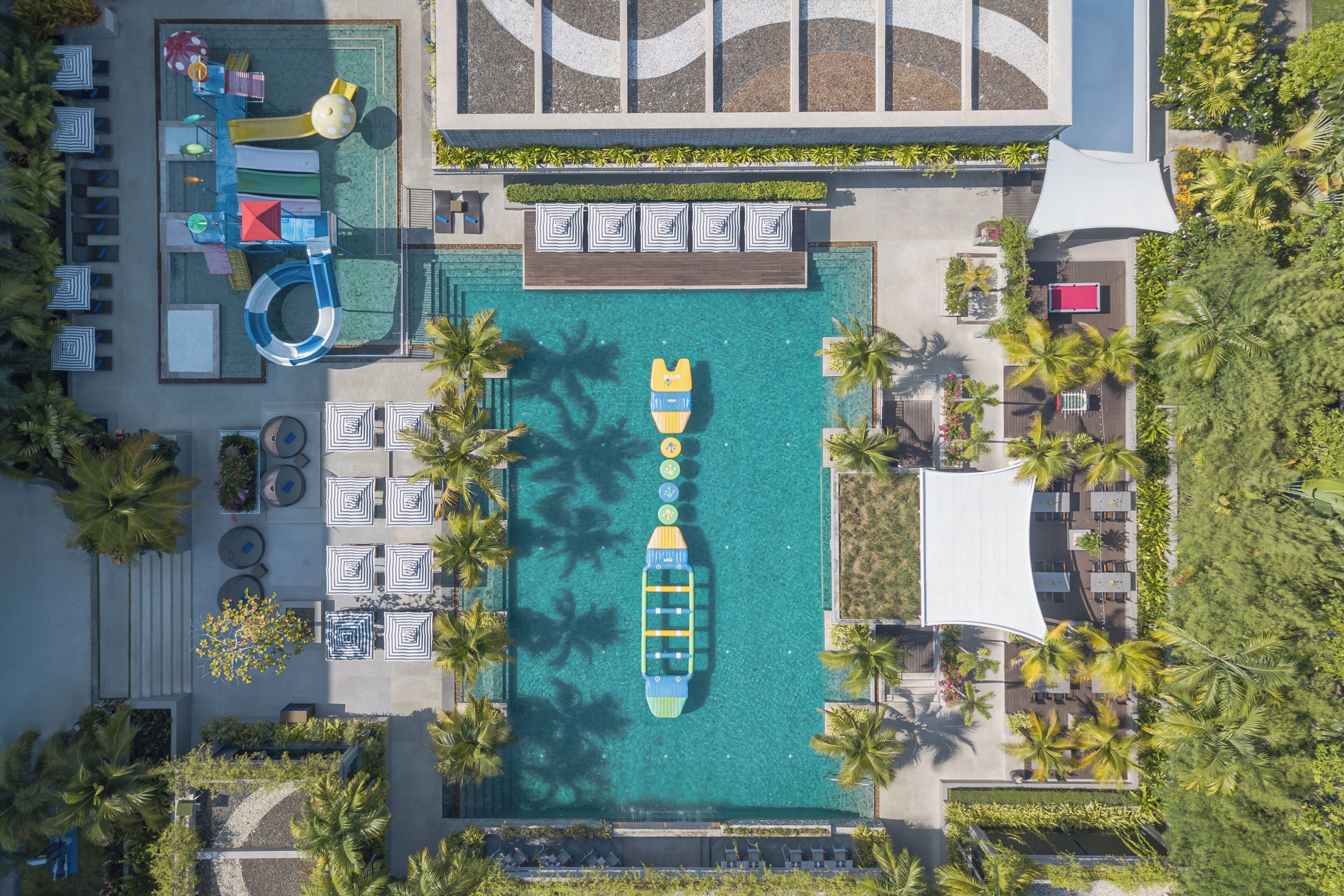 An aerial view of a resort with a swimming pool, lounge chairs, and palm trees.