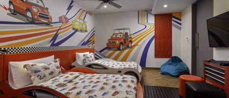 Habitación infantil con temática de carreras, que incluye una cama, dos camas individuales, un ventilador de techo, un televisor y un sillón de peluche.