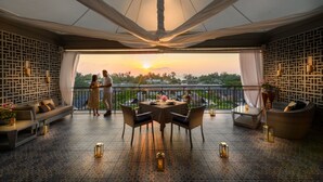 Una terraza con mesa y sillas, un sofá y un balcón con vista al atardecer.