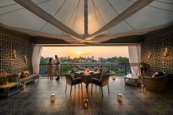 Une terrasse avec une table et des chaises pour les repas, un canapé et un balcon offrant une vue sur le coucher de soleil.