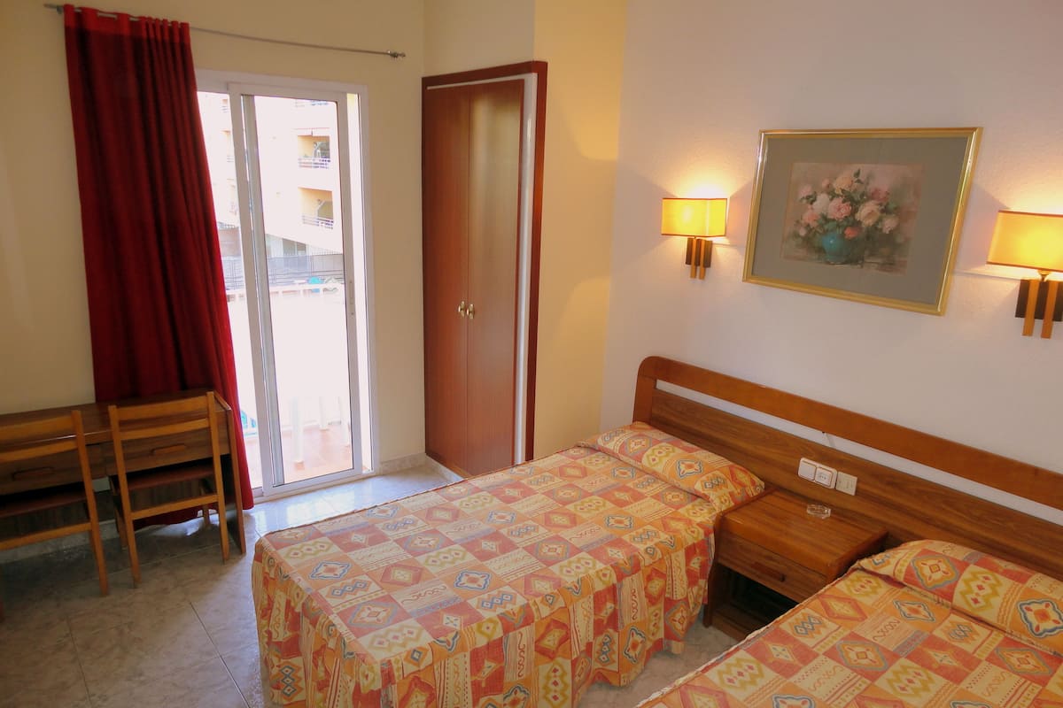 A hotel room with two beds, a desk, and a door leading to a balcony.