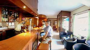 Zona de bar amb un barman servint begudes, un espai d'estar amb cadires i vista al carrer.