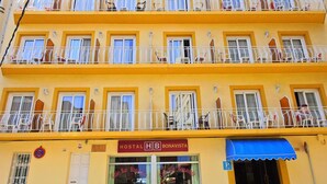 Un edifici de diverses plantes amb balcons, un cartell que indica que és un hostal i una tenda blava sobre l'entrada.