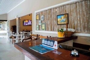 A hotel reception area with a wooden reception desk, a television mounted on the wall, and framed awards on the wall. - Vila Pitanga (Búzios)