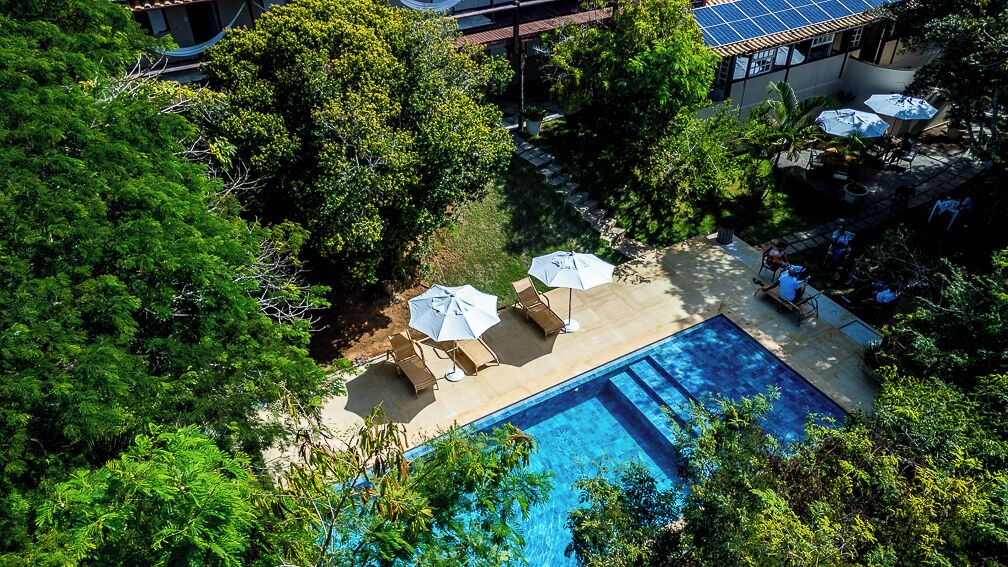 An aerial view of a hotel with a swimming pool surrounded by lush greenery and outdoor seating.