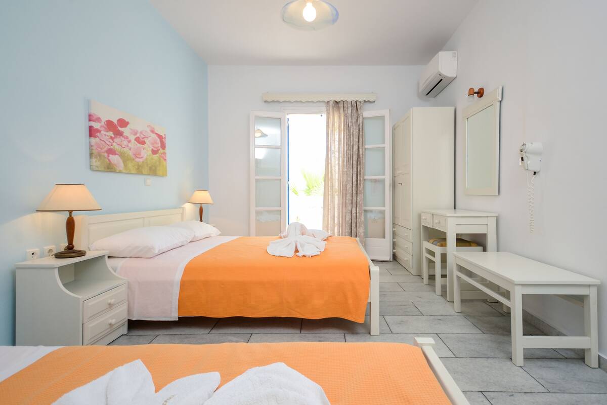 A bedroom with two beds, a desk, a wardrobe, and a bathroom visible through an open door.