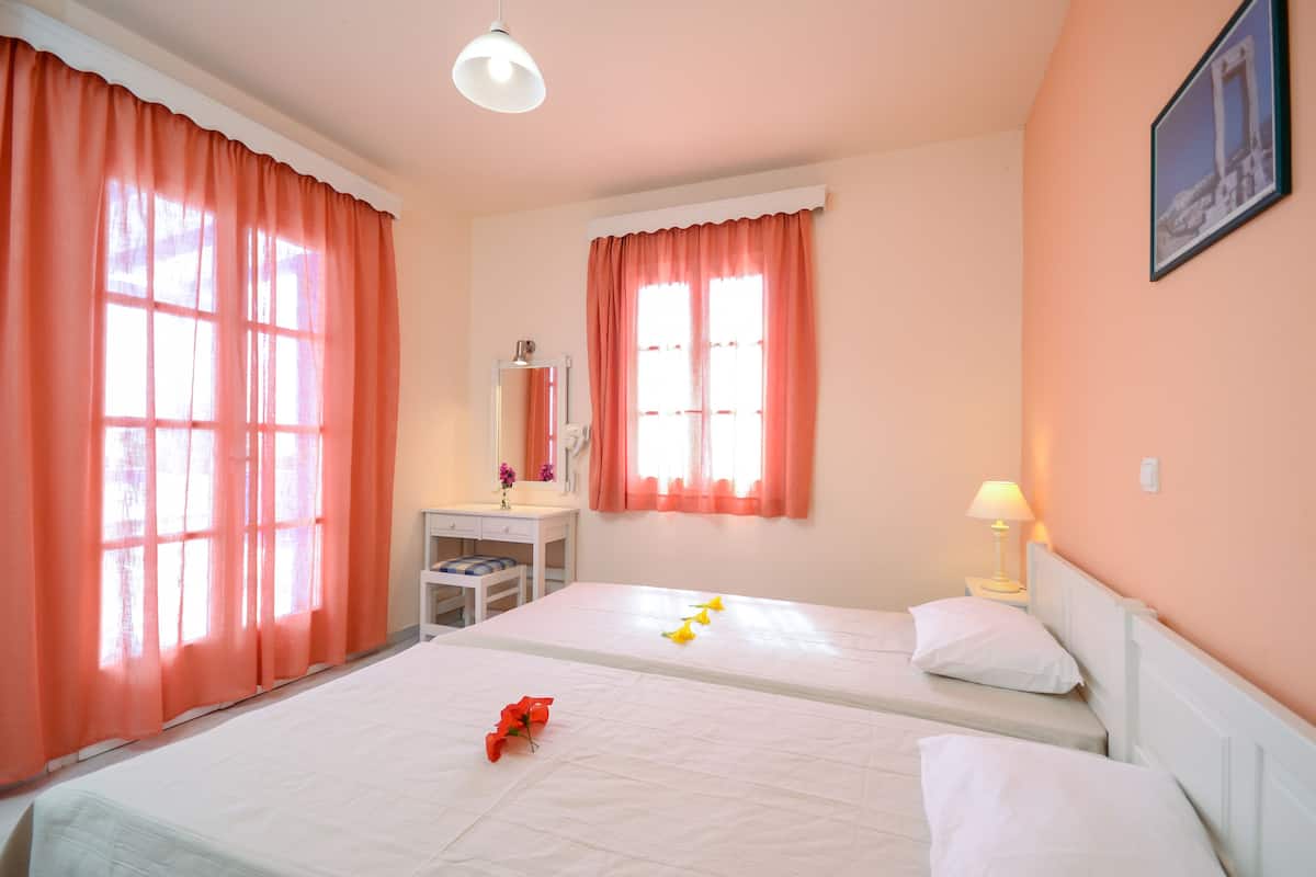 A hotel room with two beds, a desk, a chair, a lamp, and a picture on the wall.