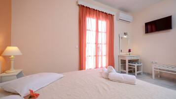 A hotel room with a bed, a bedside table with a lamp, a vanity with a mirror, and a TV mounted on the wall.