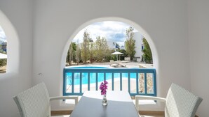 A balcony with a view of a swimming pool, white walls, and a table with a vase of flowers. - Hotel Francesca (Naxos)