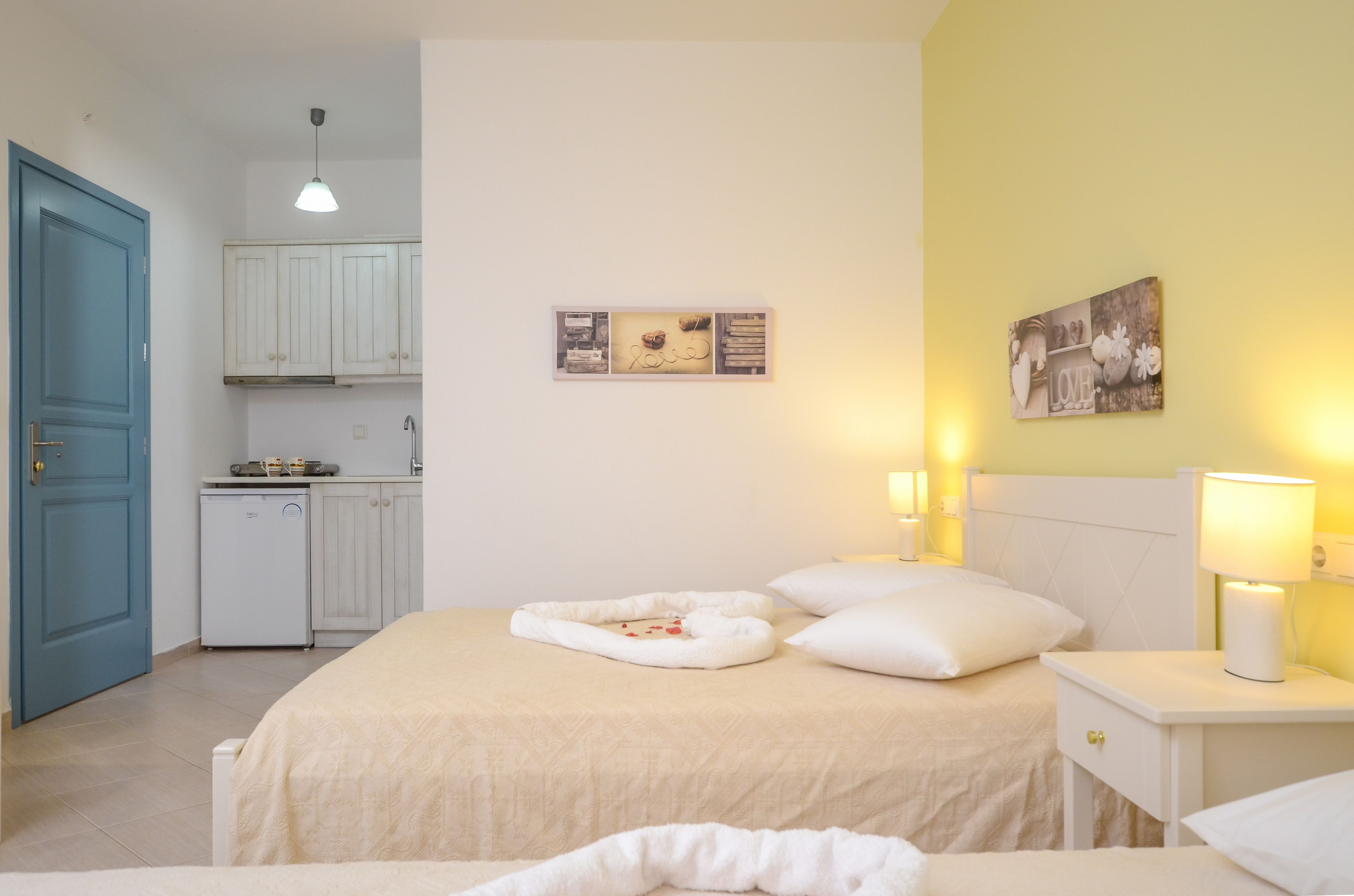 A bedroom with a bed, bedside tables, and a small kitchenette.