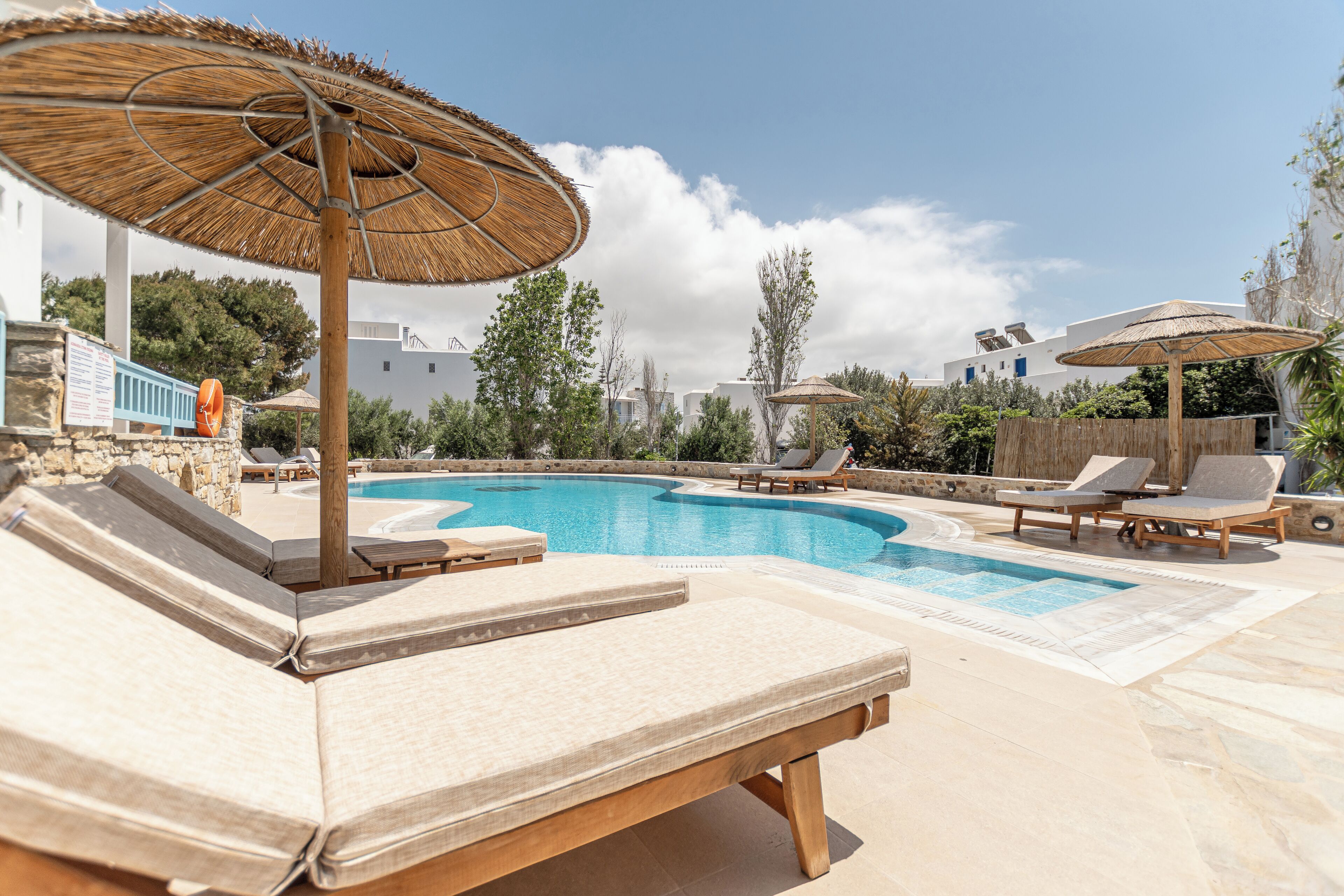 Un área junto a la piscina con sillones de descanso y sombrillas, piscina azul cristalina y un muro de piedra al fondo.