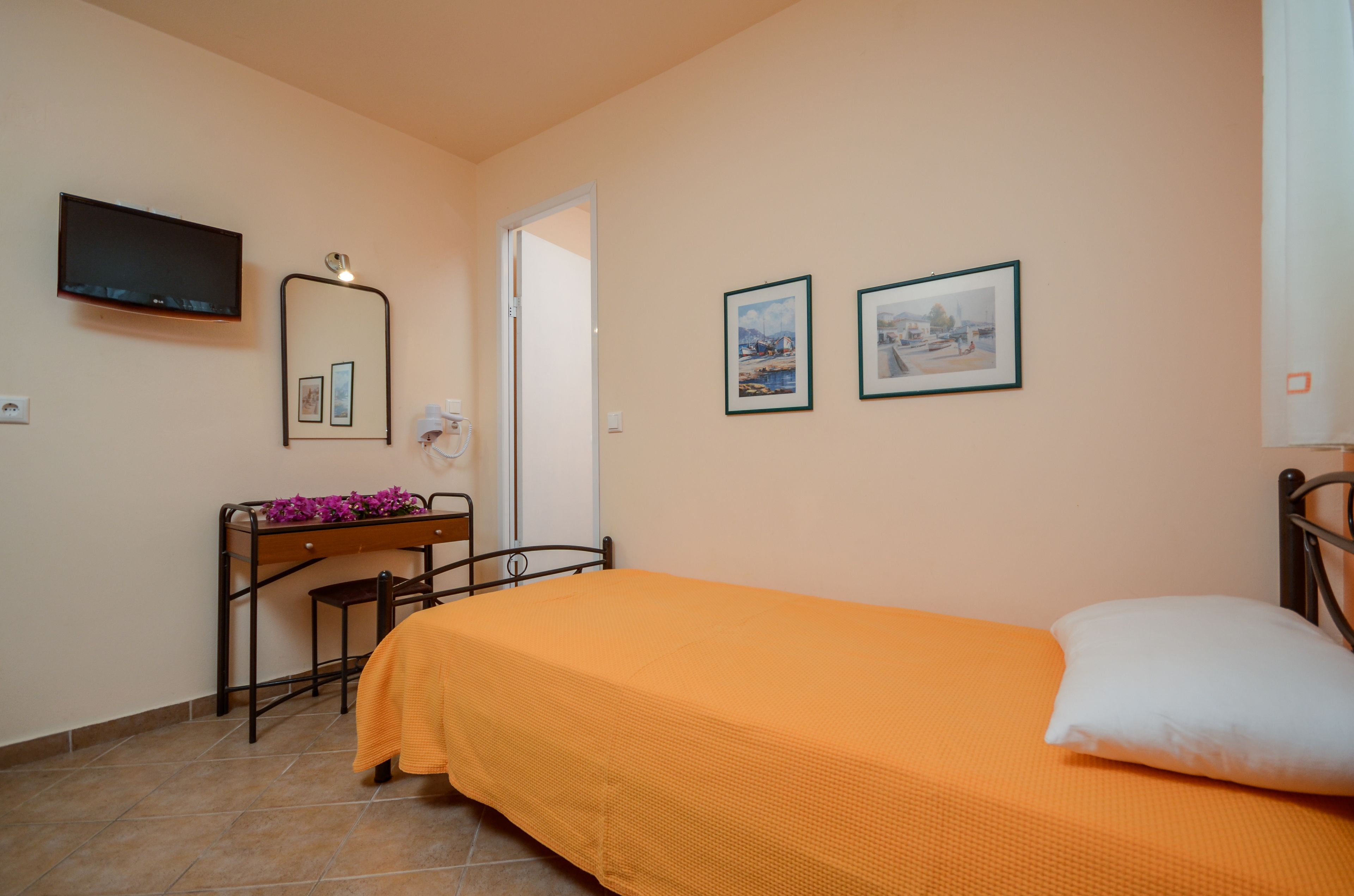 A bedroom with a bed, a desk with a chair, a television, and two framed pictures on the wall.
